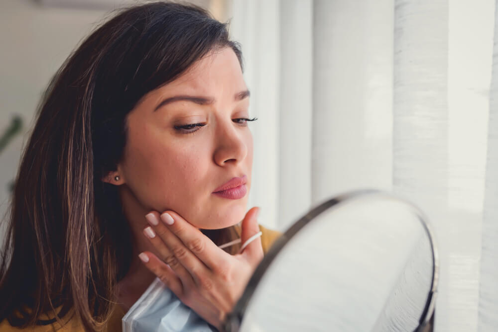 Woman looking at maskne in mirror